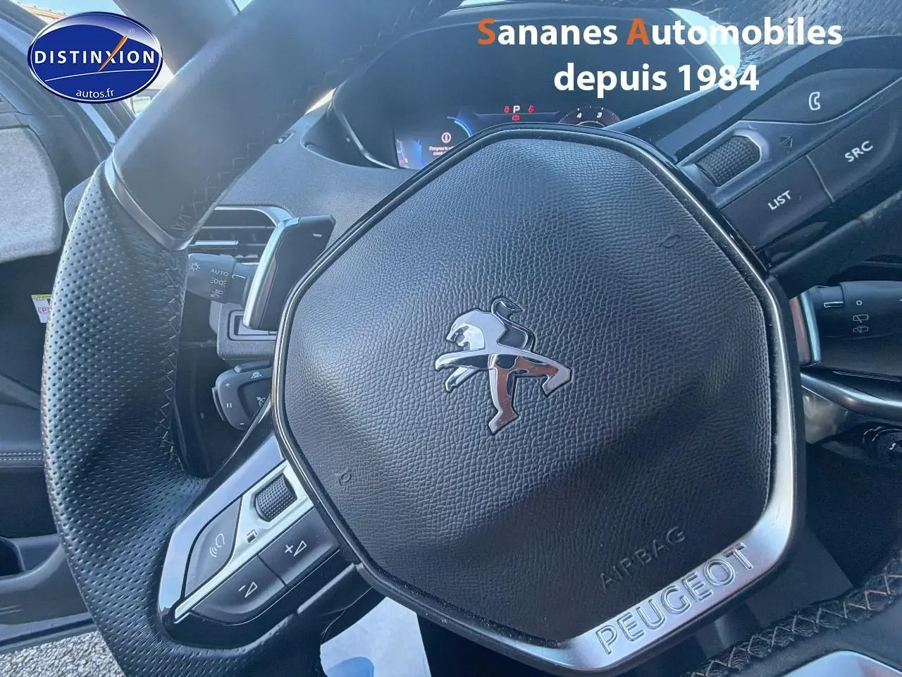 Gros plan sur le volant cuir perforé Peugeot du 3008 2023, avec commandes intégrées et badge chromé GT.