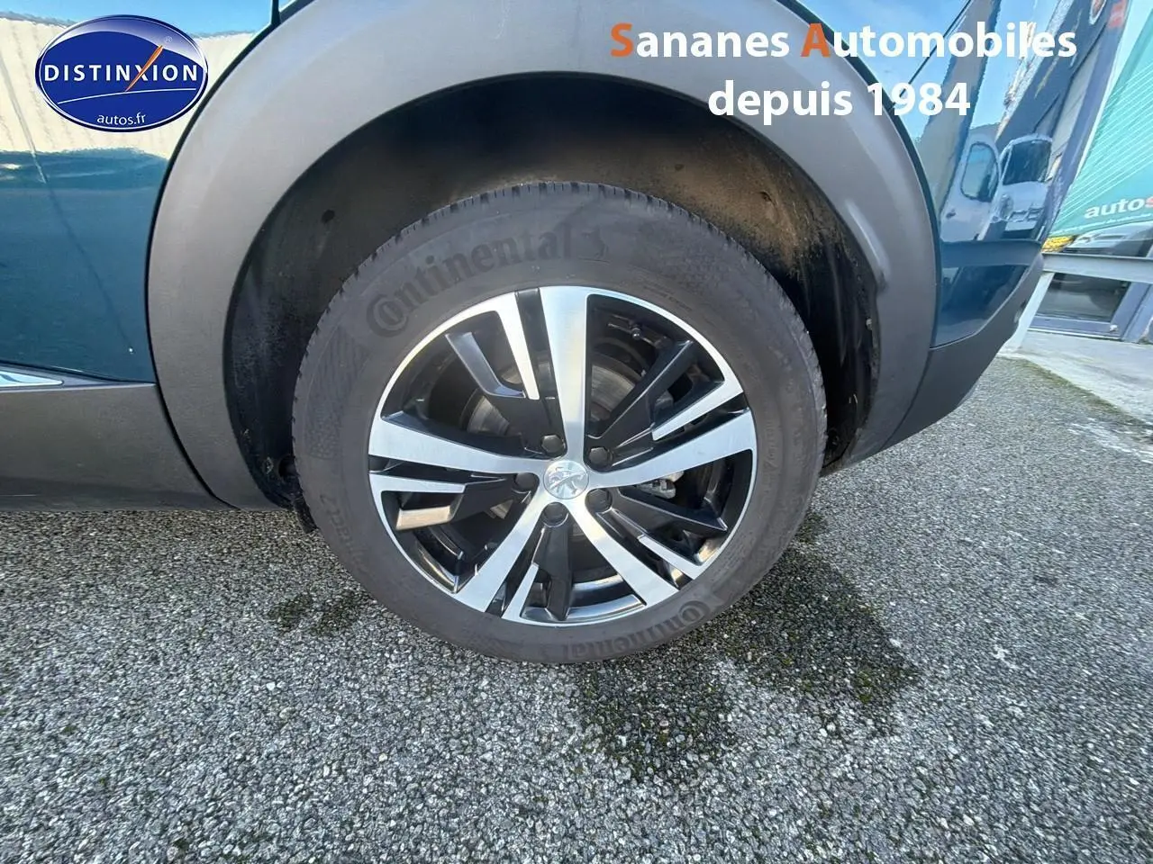 Gros plan sur la roue avant droite du Peugeot 3008 bleu avec jante alliage bicolore et logo Peugeot central.