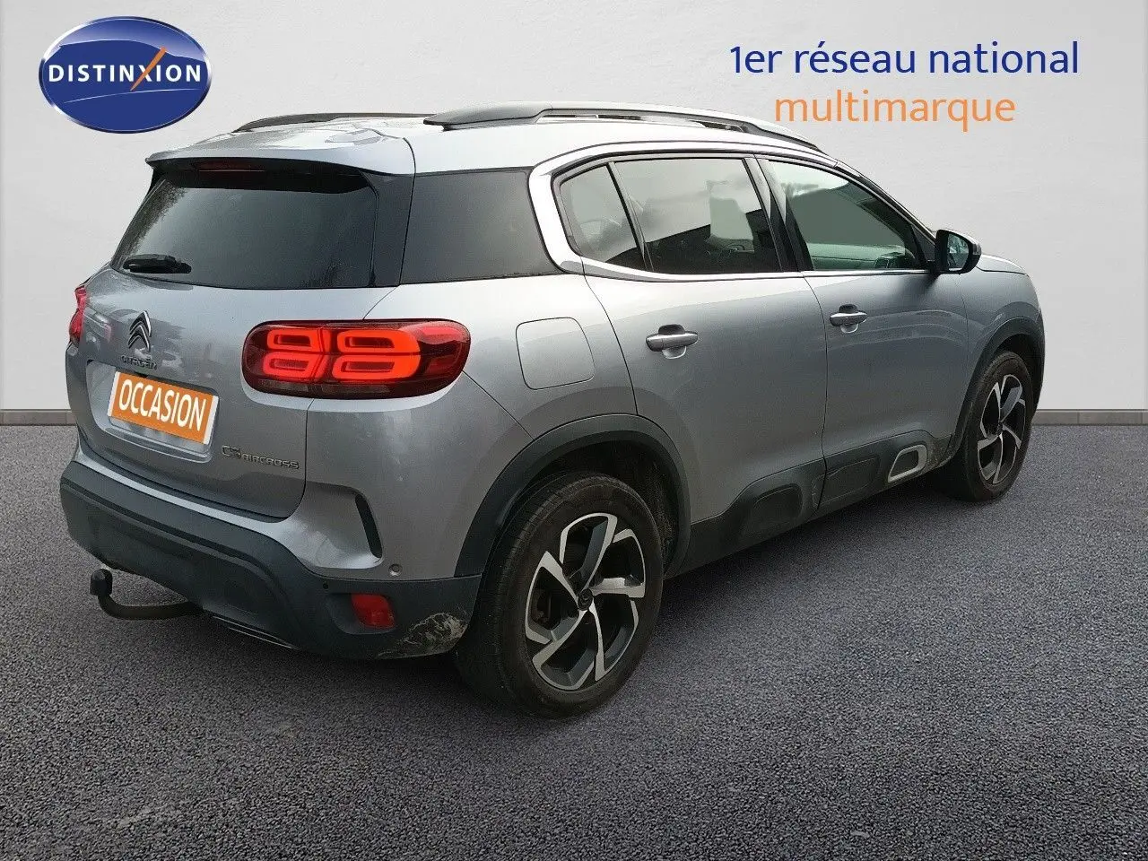 Vue 3/4 arrière droite d'un Citroën C5 Aircross gris Artense métallisé avec feux arrière allumés et attelage visible.