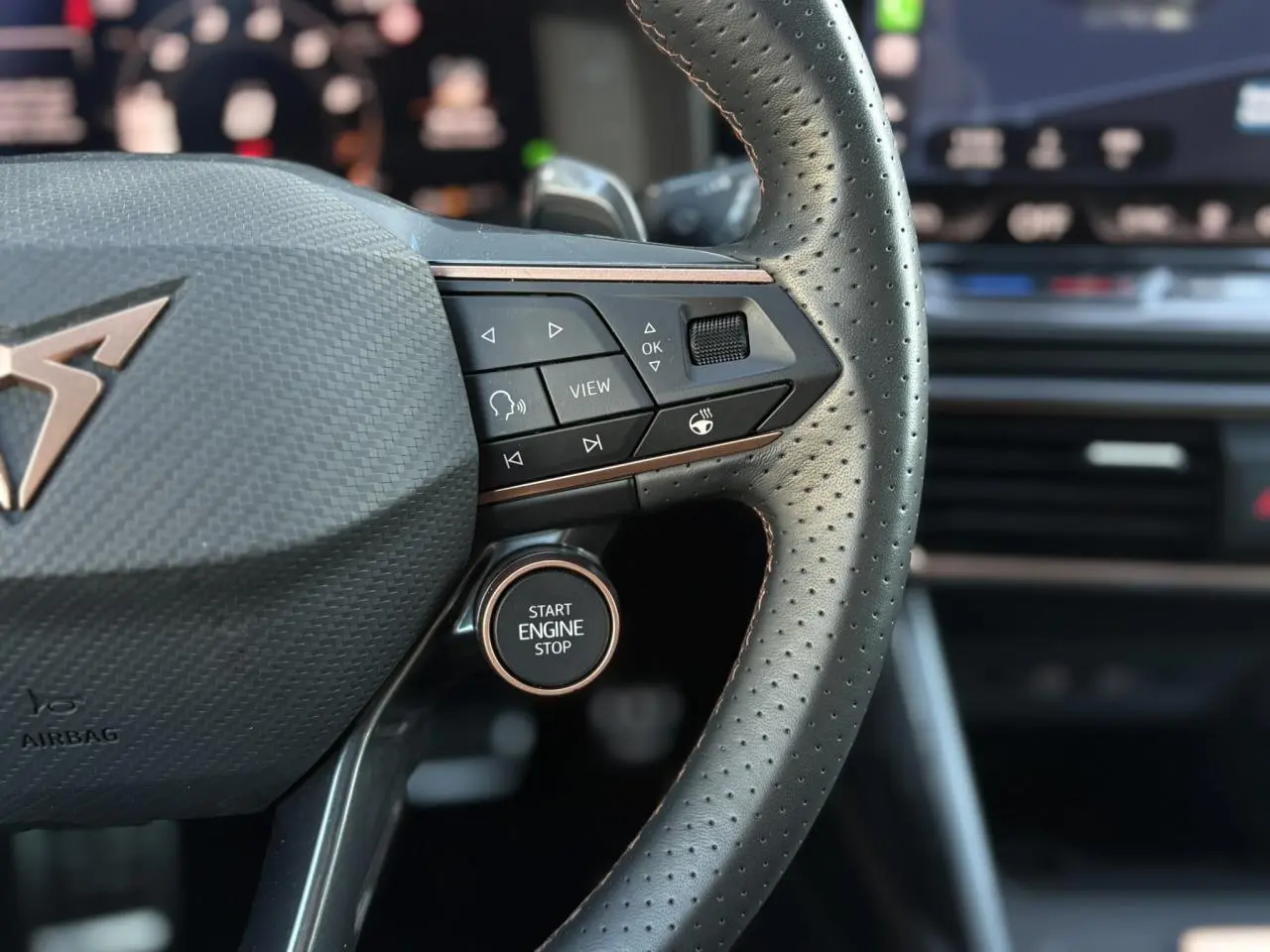 Gros plan sur le volant cuir perforé noir de la CUPRA Leon 2025 avec bouton start engine stop et commandes intégrées.