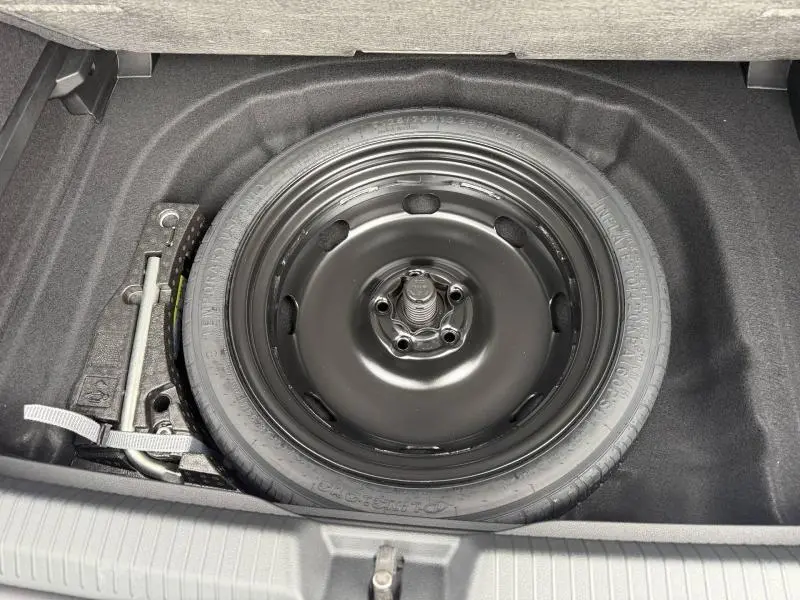 Vue plongeante sur la roue de secours noire et les outils de bord dans le coffre d'une Volkswagen Golf 2.0 TDI 150ch R-Line blanc nacré.