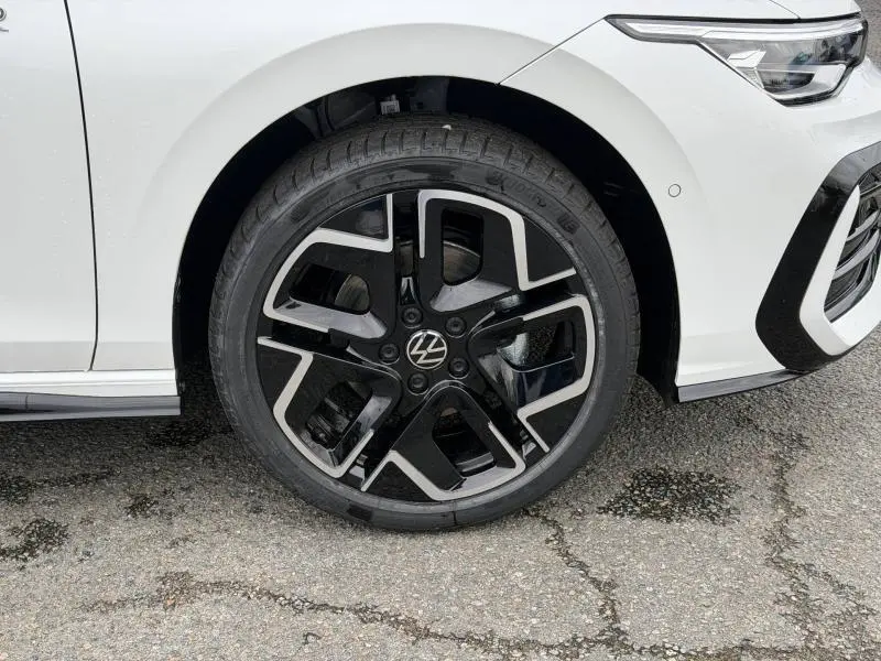 Gros plan sur la roue avant gauche d'une Volkswagen Golf 2.0 TDI R-Line blanche nacrée avec jante noire et argentée.