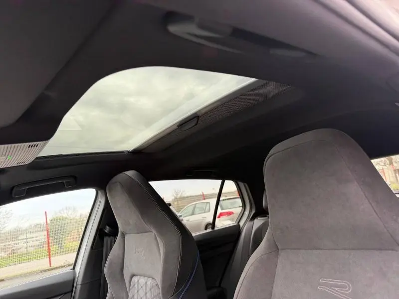 Vue intérieure montrant les sièges avant en alcantara gris avec logo R et toit ouvrant panoramique du Volkswagen Golf blanc Oryx.