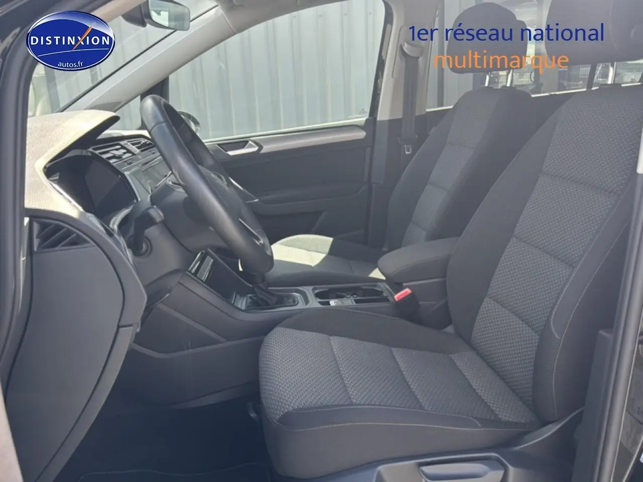 Vue intérieure côté conducteur du Volkswagen Touran 2025 noir, sièges tissu gris et volant cuir multifonction.