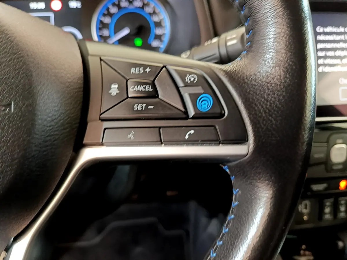Gros plan sur le côté gauche du volant cuir noir de la Nissan Leaf blanche, avec commandes de régulateur et assistance.