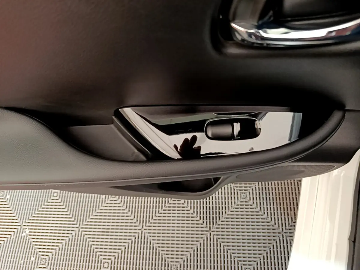 Poignée intérieure noire côté gauche de la porte avant d'une Nissan Leaf blanche, avec reflet visible sur la surface brillante.