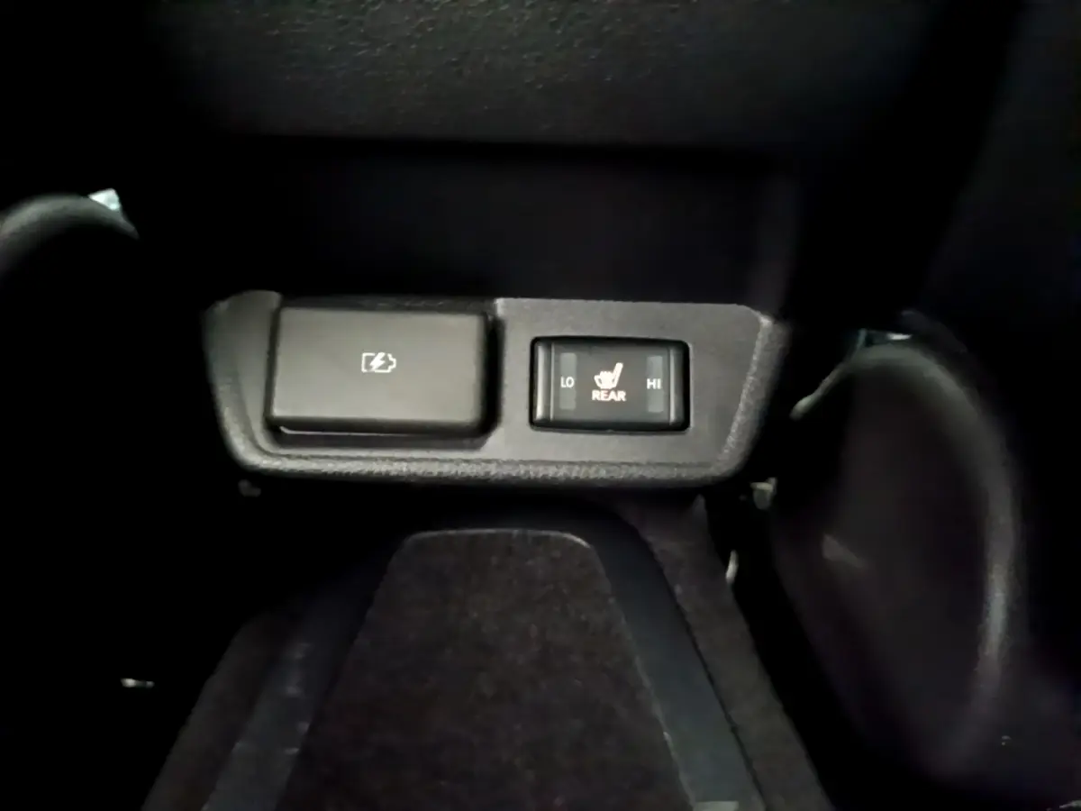 Gros plan sur les commandes de chauffage des sièges arrière et prise électrique dans l'habitacle noir d'une Nissan Leaf blanche.