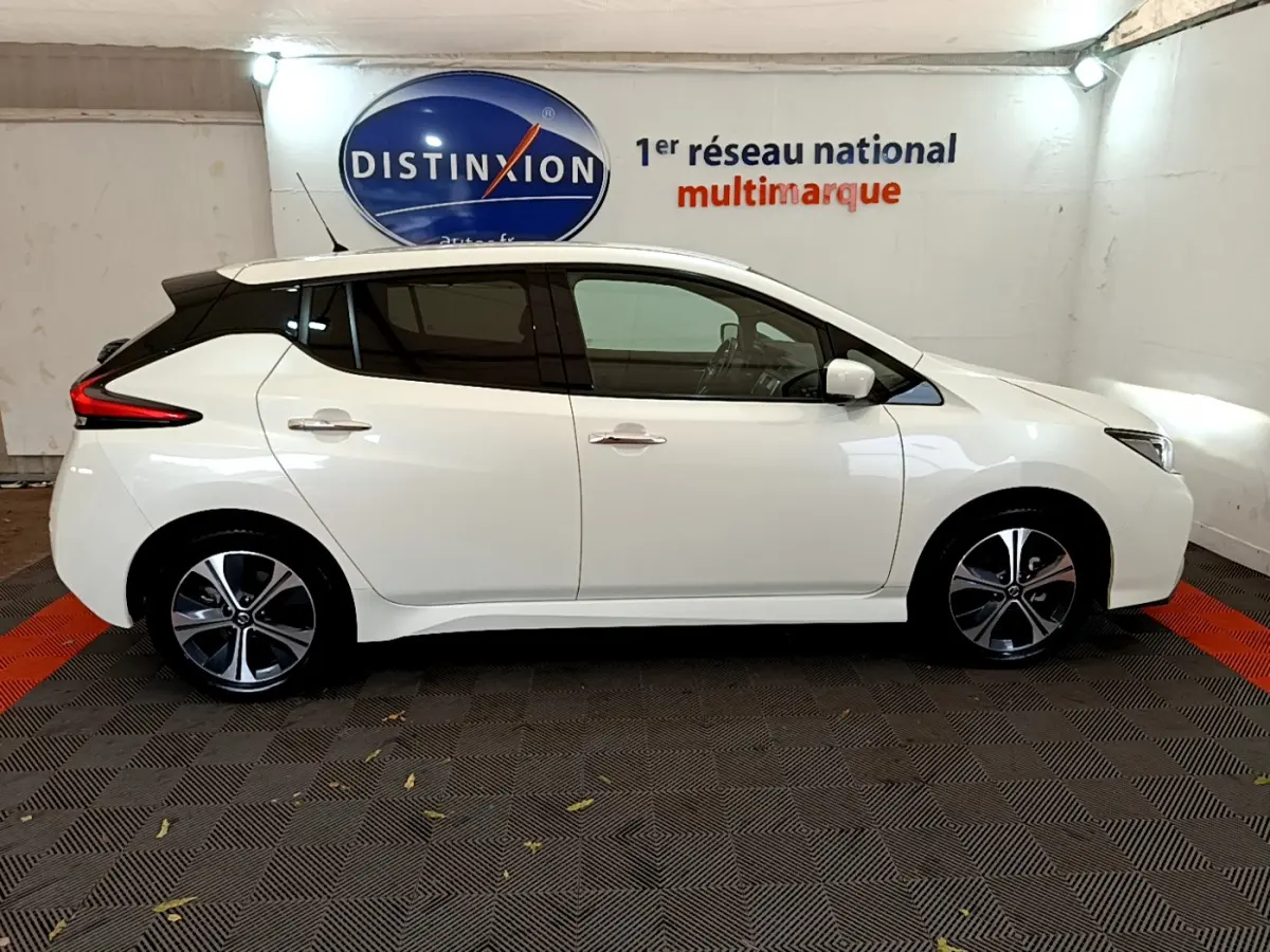 Profil côté gauche d'une Nissan Leaf électrique blanche 2020, avec jantes modernes et vitres teintées, en intérieur showroom.