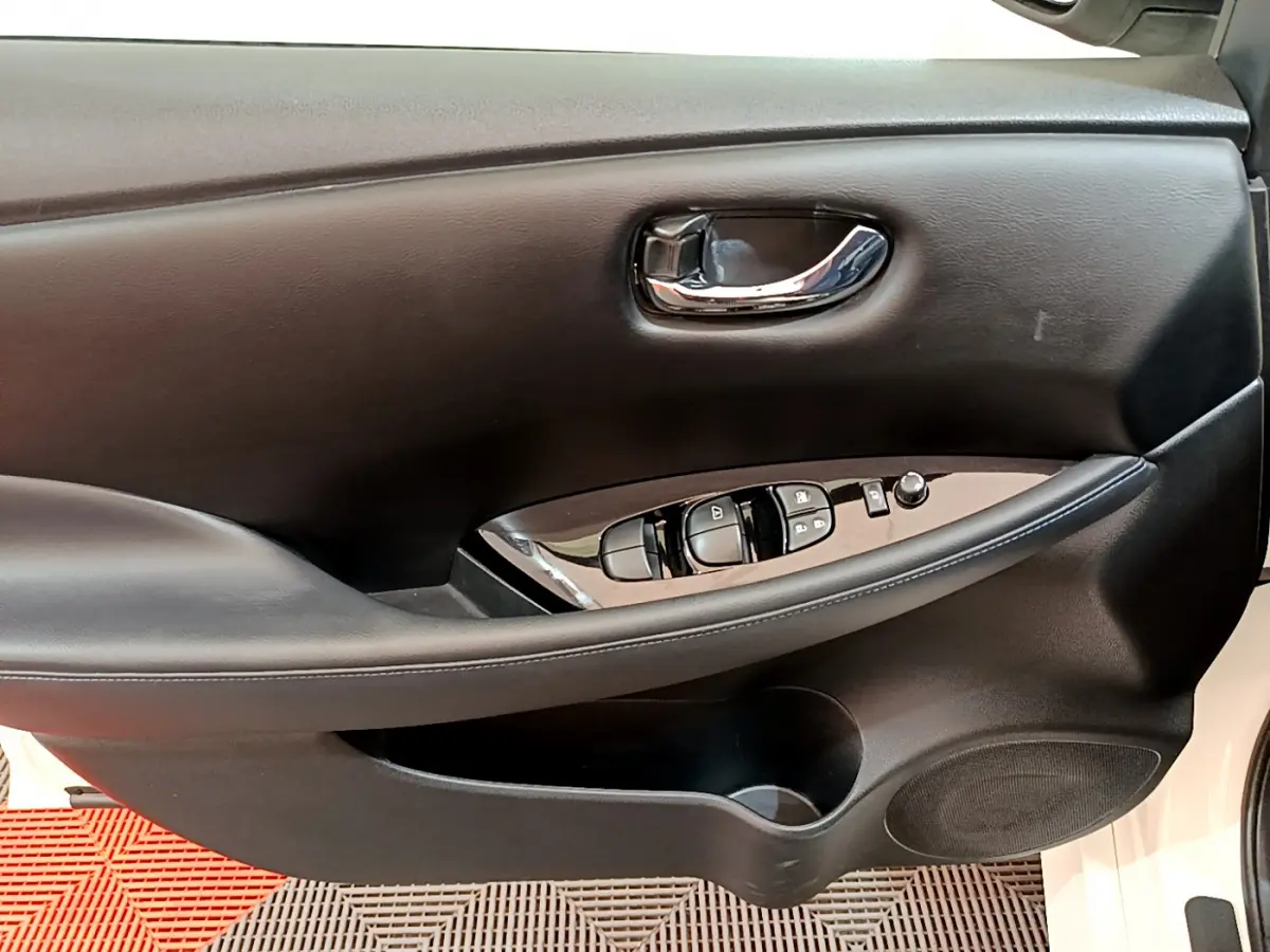 Intérieur côté conducteur de la porte noire d'une Nissan Leaf blanche, avec commandes électriques et poignée chromée.