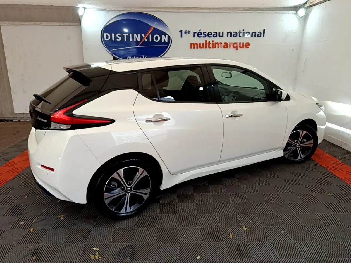 Vue 3/4 arrière droite d'une Nissan Leaf blanche avec toit noir et jantes alliage dans un showroom intérieur.