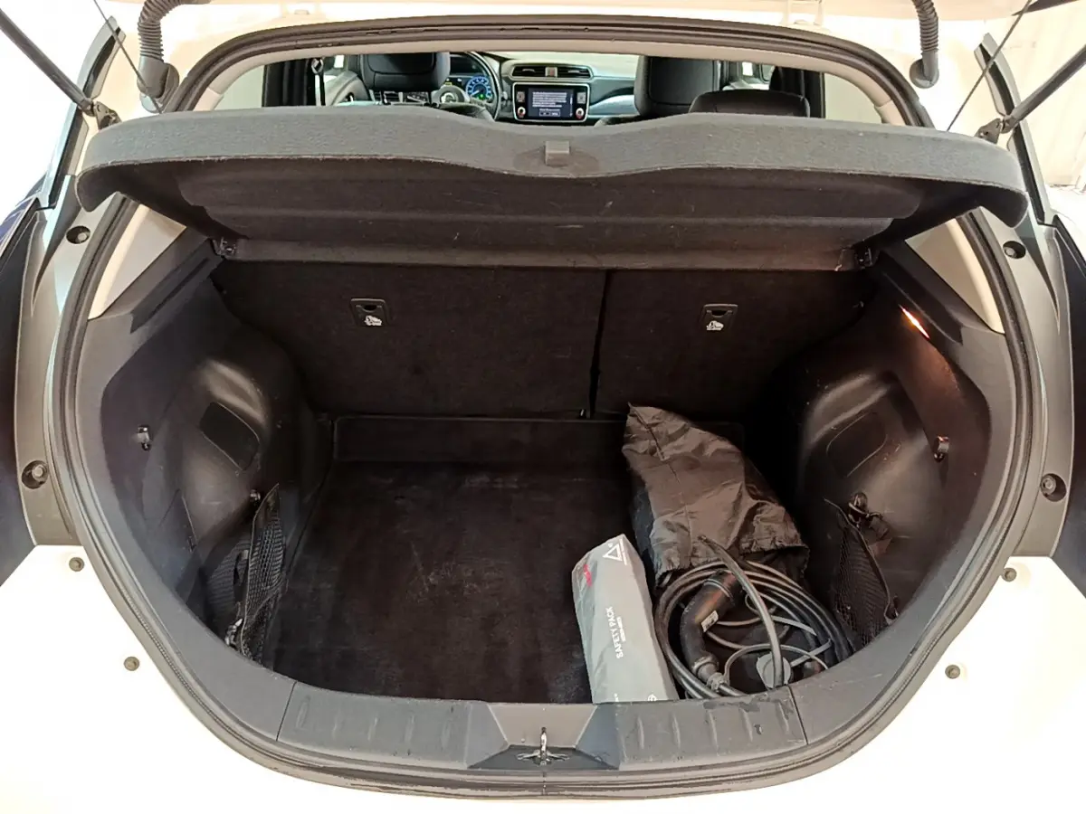 Coffre ouvert d'une Nissan Leaf blanche 2020, vue arrière montrant câble de recharge et tablette de séparation.
