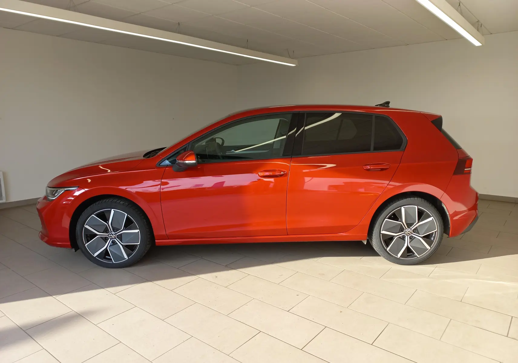 Profil côté gauche d'une Volkswagen Golf 2.0 TDI 150 DSG7 Style rouge métallisé avec jantes alliage 18 pouces dans un showroom.