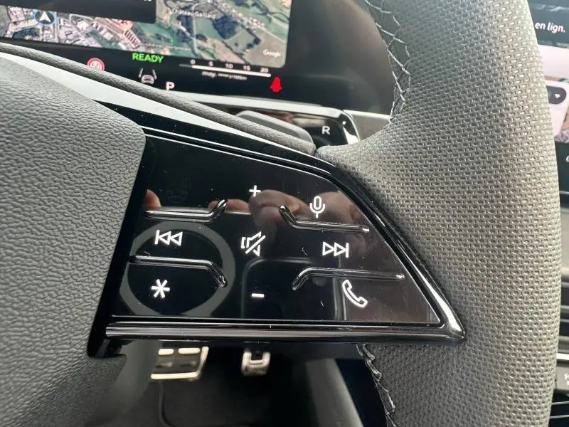 Gros plan sur les commandes multifonctions au volant de l'Audi Q3 gris 2026, avec écran de navigation en arrière-plan.