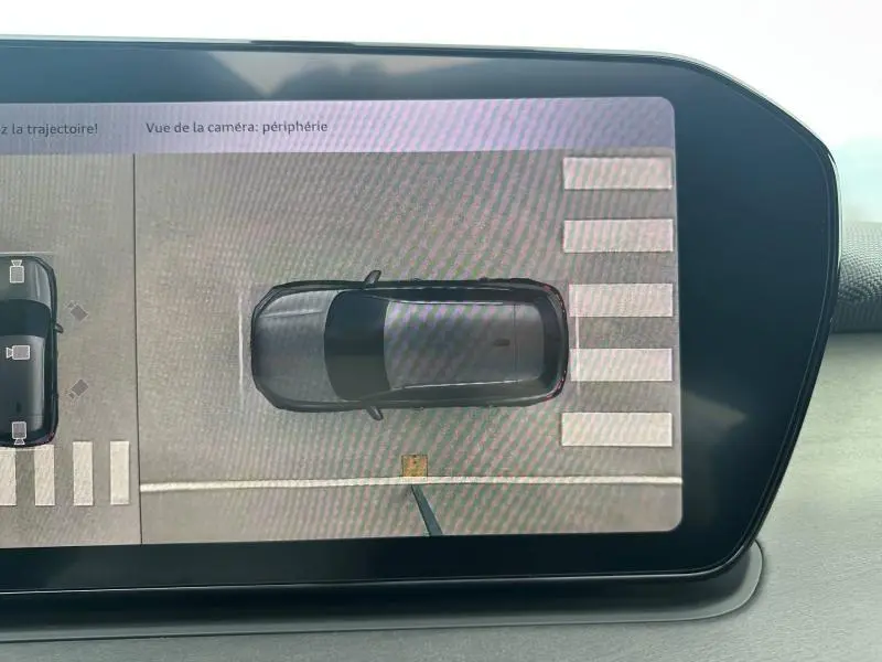 Vue aérienne sur l'écran du tableau de bord montrant un Audi Q3 gris en stationnement sur un passage piéton.