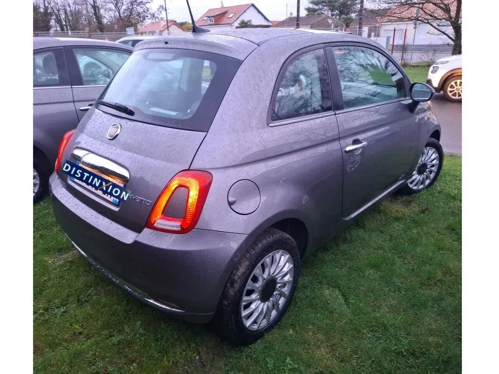 Vue 3/4 arrière droite d'une FIAT 500 2022 gris Electroclash avec feux arrière allumés sur pelouse humide.