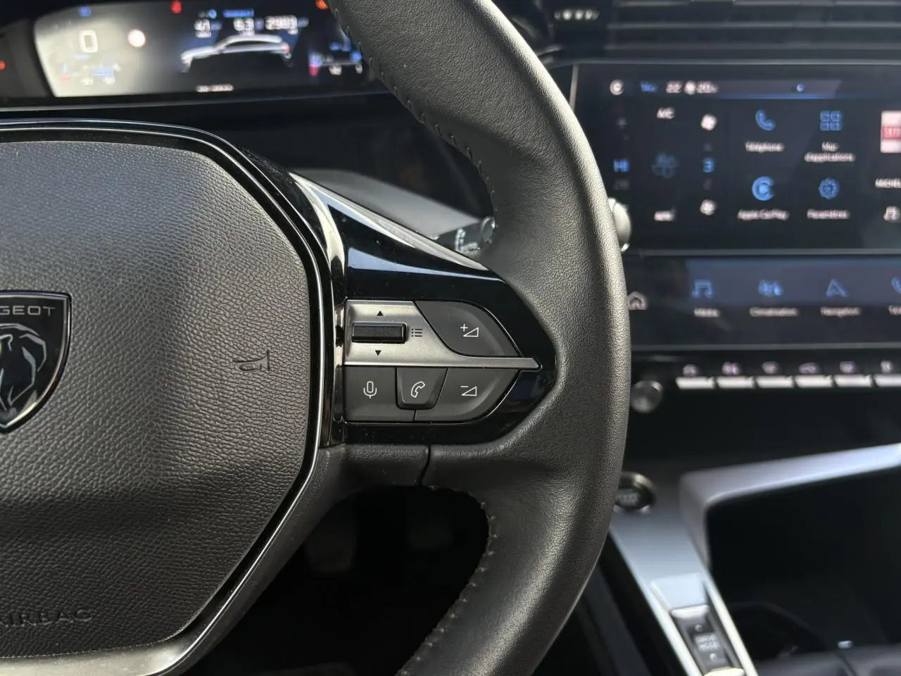 Gros plan sur le volant en cuir noir de la Peugeot 308 2024 avec commandes intégrées et tableau de bord numérique en arrière-plan.