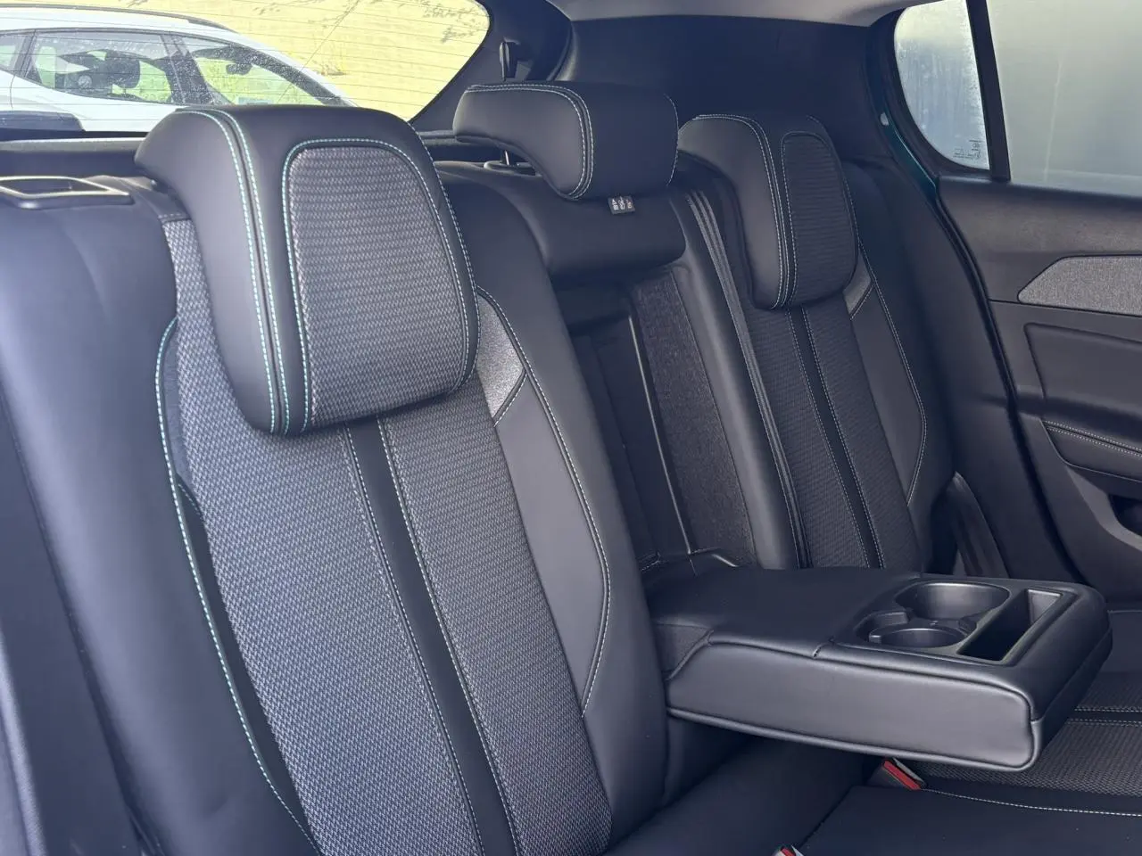 Vue intérieure des sièges arrière de la Peugeot 308 2024, sellerie tri matières noire avec surpiqûres bleues et accoudoir central déployé.