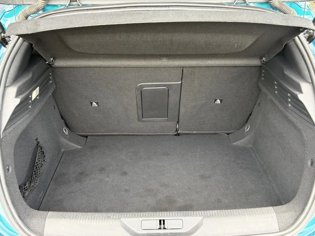 Coffre ouvert vu de l'arrière d'une Peugeot 308 2024 Bleu Obsession avec intérieur noir et filet de rangement latéral.