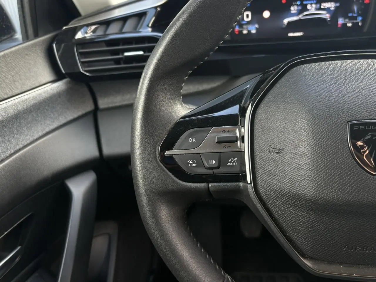 Gros plan sur le volant cuir noir de la Peugeot 308 2024 avec commandes intégrées et tableau de bord numérique.