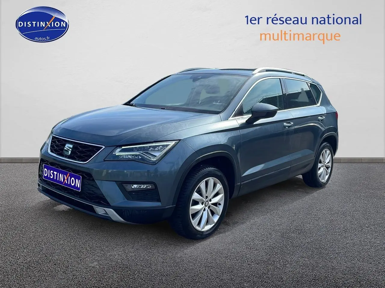 SEAT Ateca bleu/gris en 3/4 avant droit, avec jantes alu et barres de toit visibles.
