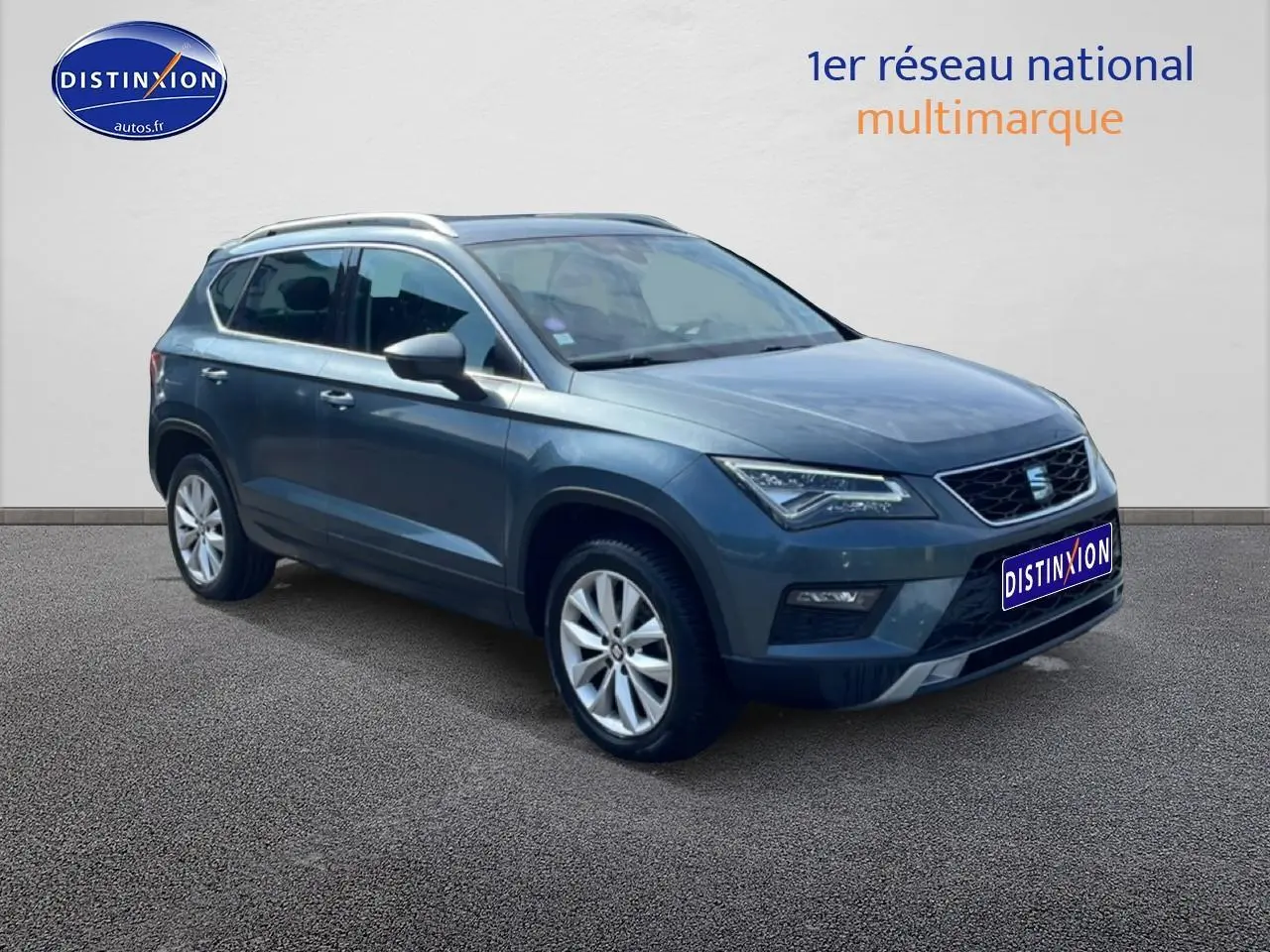 SEAT Ateca bleu/gris en 3/4 avant droit, avec jantes alu et barres de toit visibles sur fond neutre.