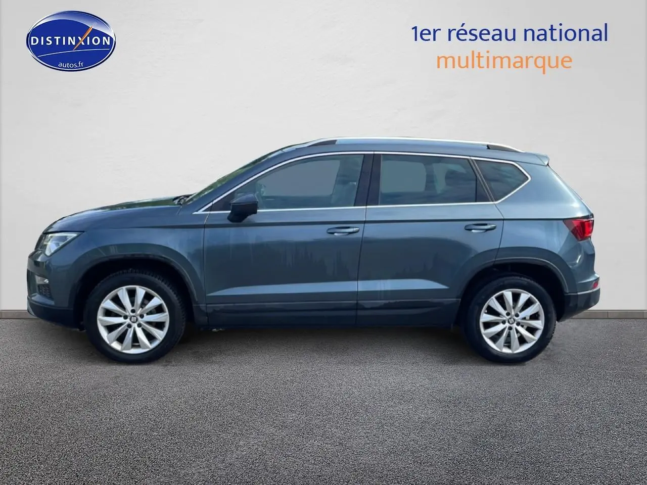 Vue de profil côté gauche d'un SEAT Ateca bleu/gris 2019 avec jantes alliage et barres de toit.