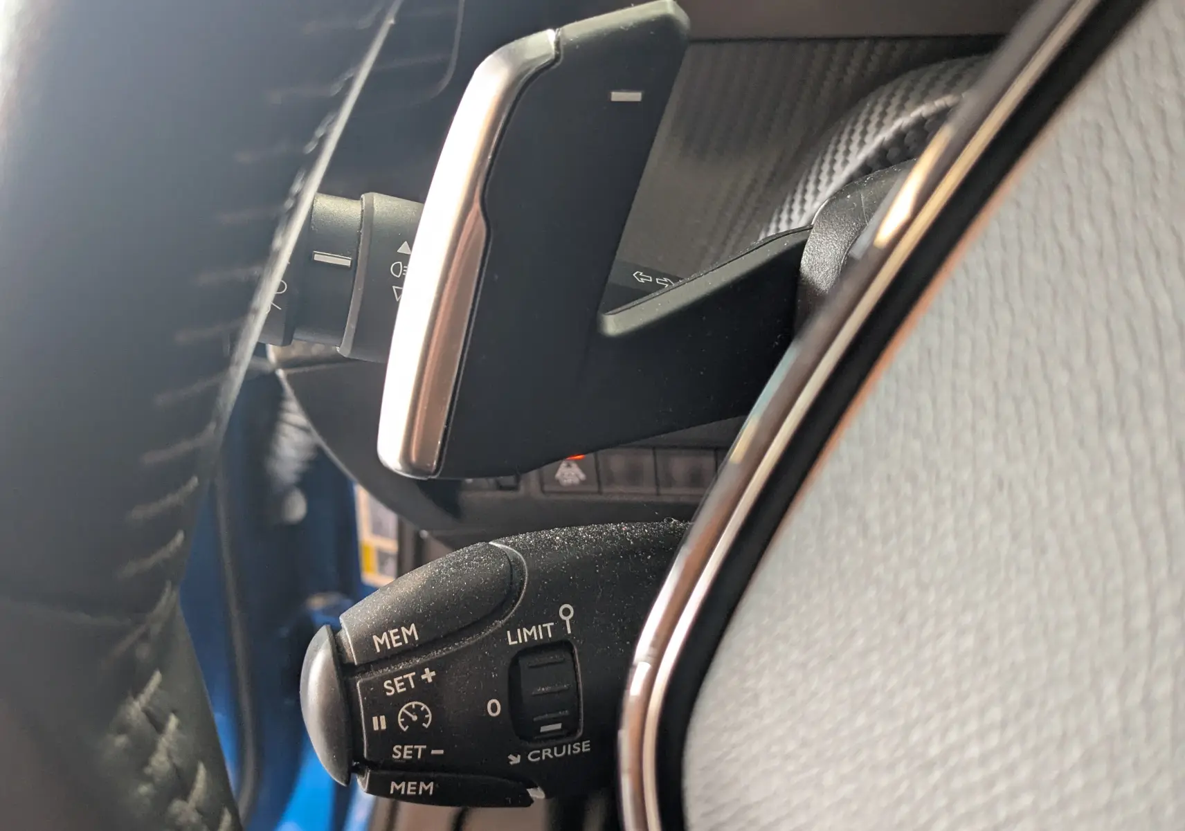 Gros plan sur la commande de régulateur de vitesse et palettes au volant dans l’habitacle d’un Peugeot 2008 bleu.