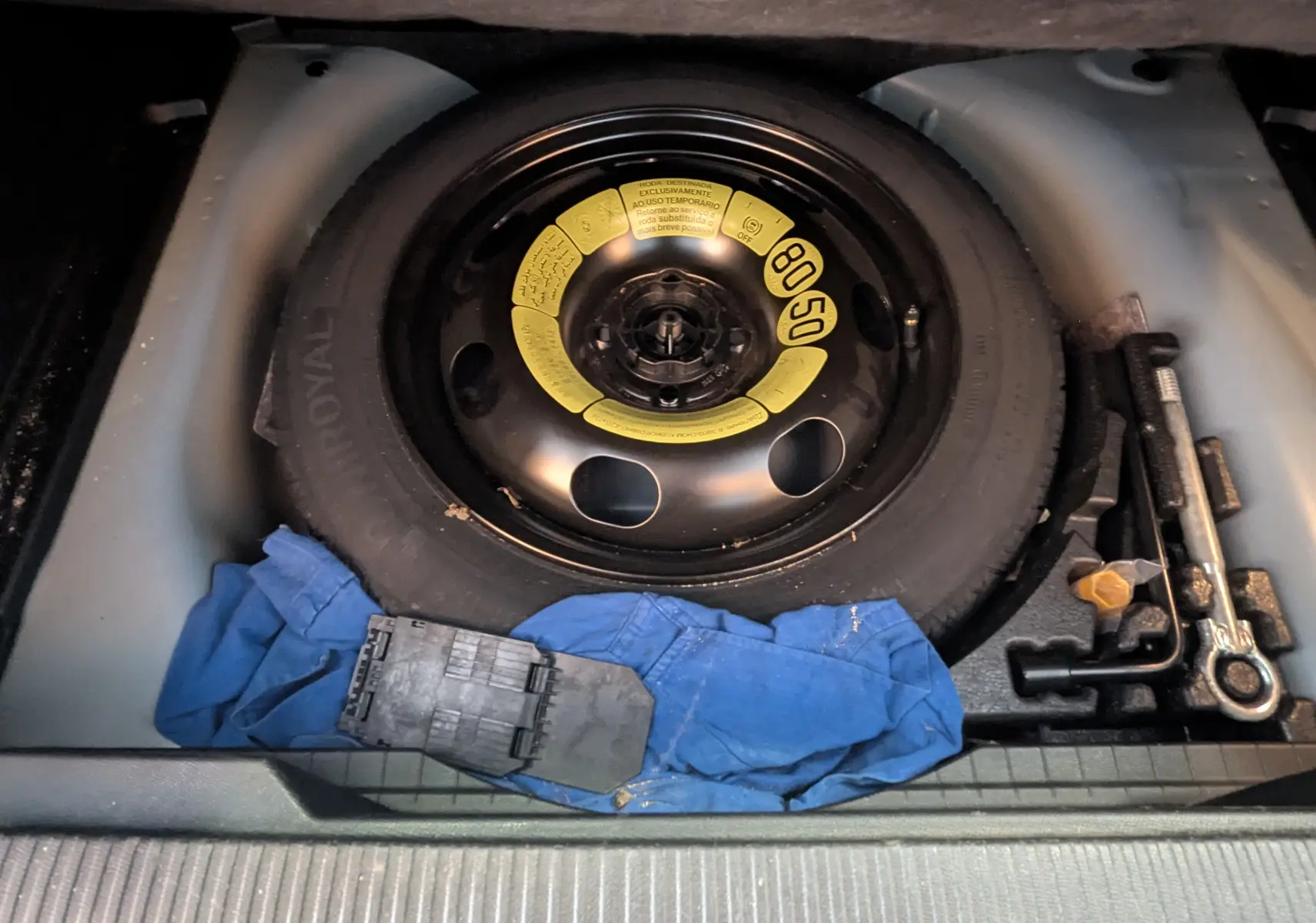 Vue rapprochée de la roue de secours noire avec étiquette jaune et outils dans le coffre d’un Peugeot 2008 bleu.