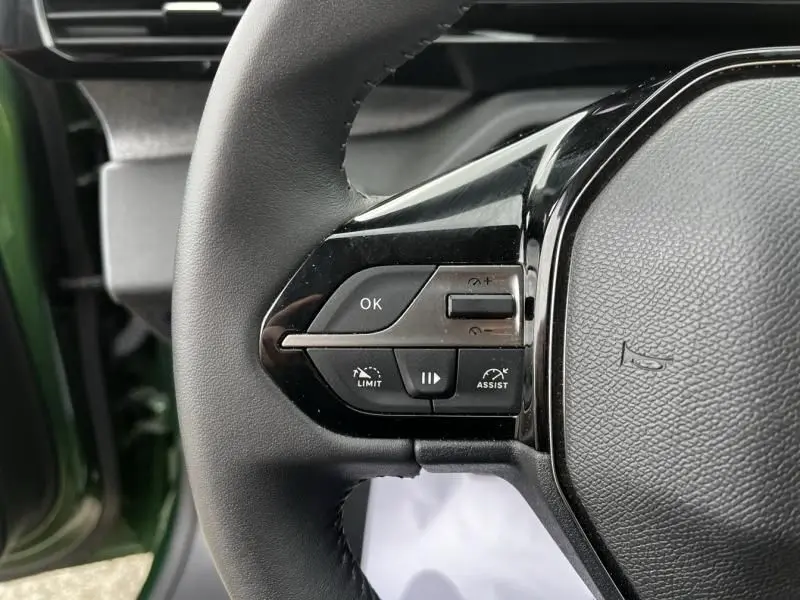 Gros plan sur les commandes gauche du volant de la Peugeot 308 1.2 PureTech 130 Allure 2023, intérieur noir, porte verte olivine ouverte.