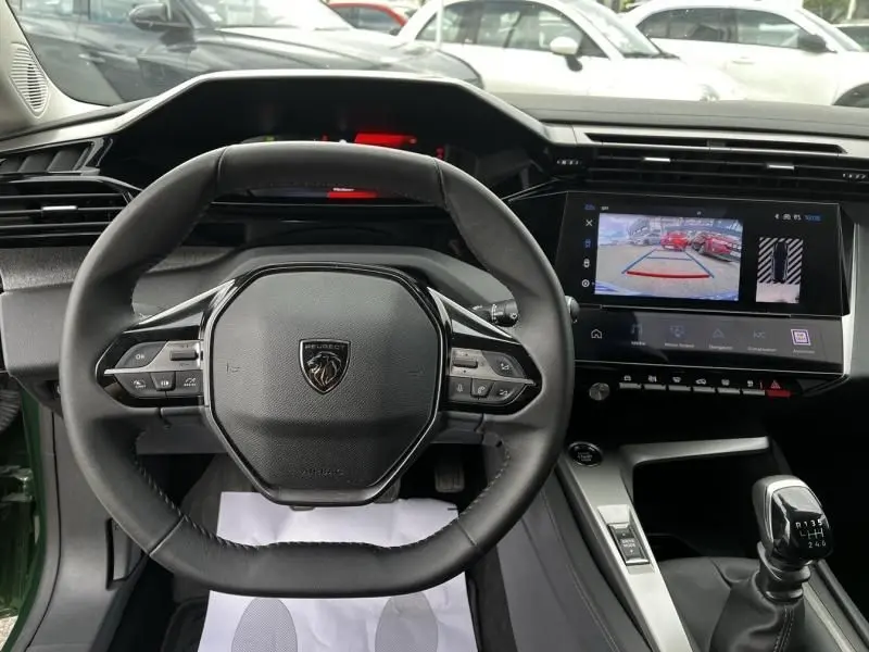 Vue intérieure centrée sur le volant Peugeot 308 vert olivine, avec tableau de bord numérique et écran multimédia affichant la caméra de recul.
