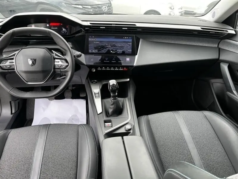 Vue intérieure avant de la Peugeot 308 1.2 PureTech 130 Allure 2023, volant compact, écran tactile central et boîte manuelle.