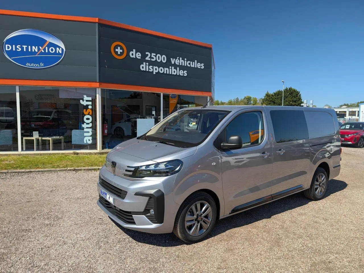 Vue 3/4 avant droit d’un Peugeot Expert Fourgon gris métallisé avec jantes alliage et vitres teintées, stationné devant un concessionnaire.