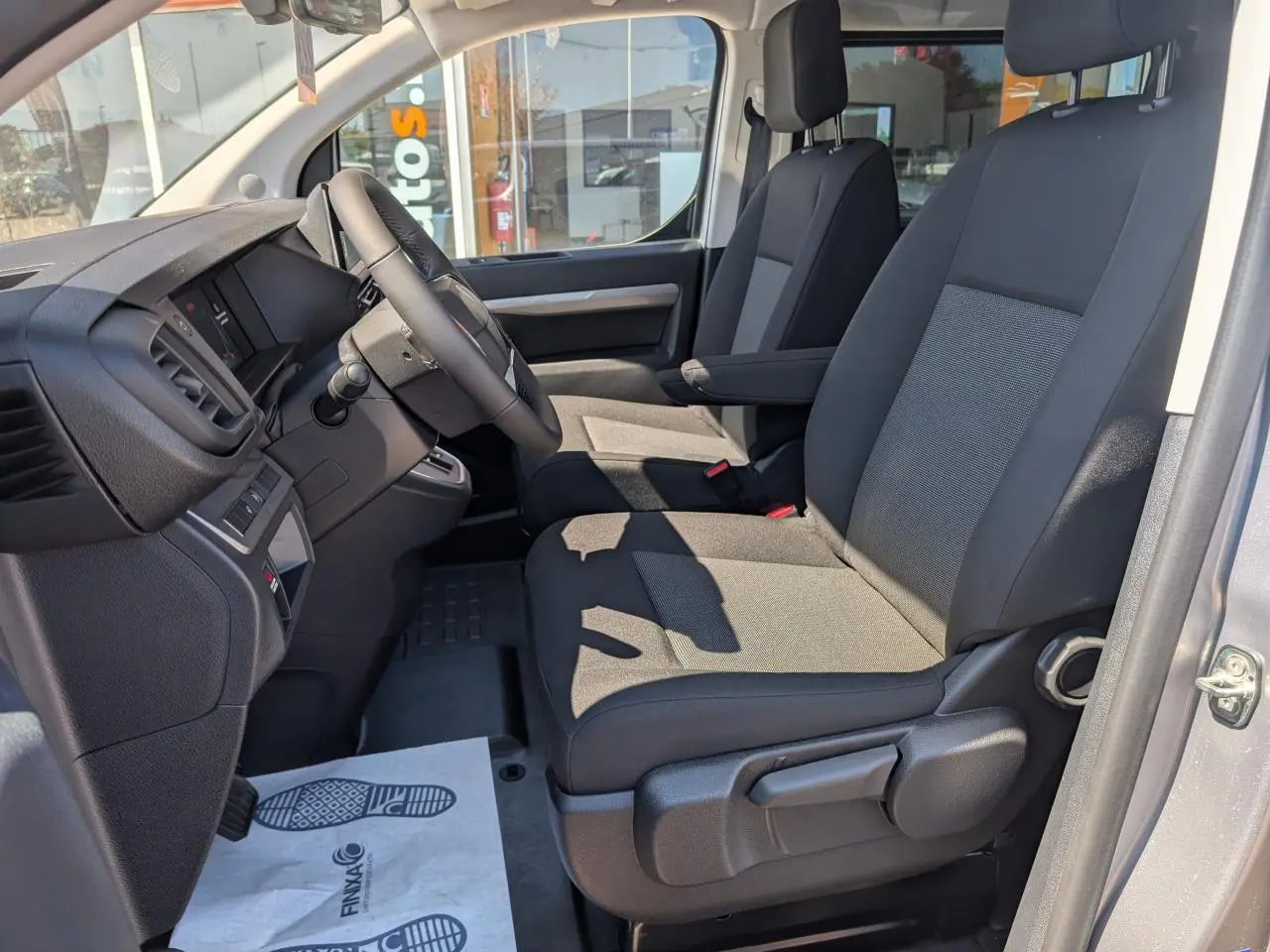 Vue intérieure côté conducteur du Peugeot Expert Fourgon XL 2026, sièges tissu bi-ton gris et noir avec accoudoirs.