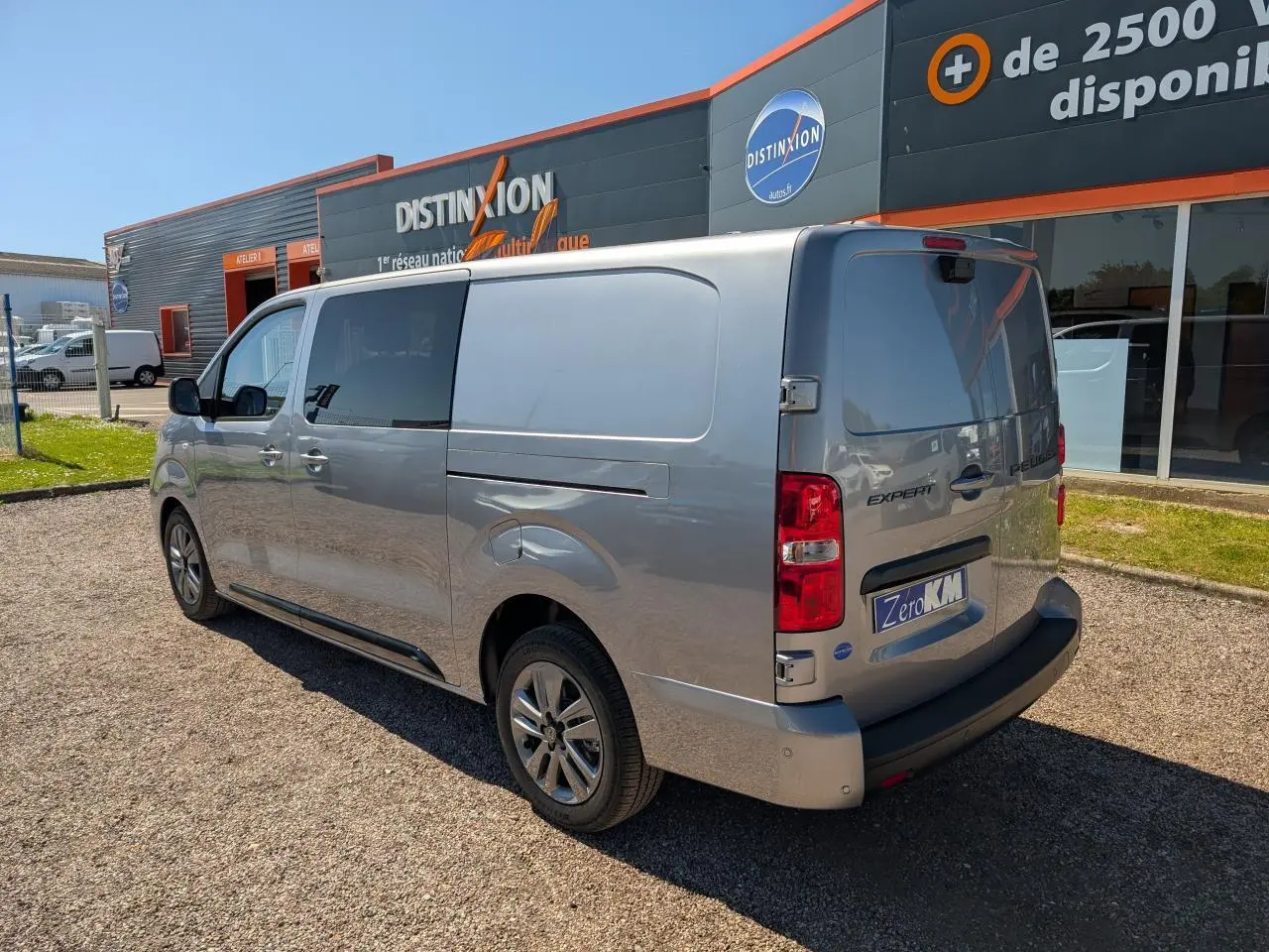 Vue 3/4 arrière droite d'un Peugeot Expert Fourgon gris métallisé avec jantes alliage 17 pouces, stationné devant un bâtiment commercial.