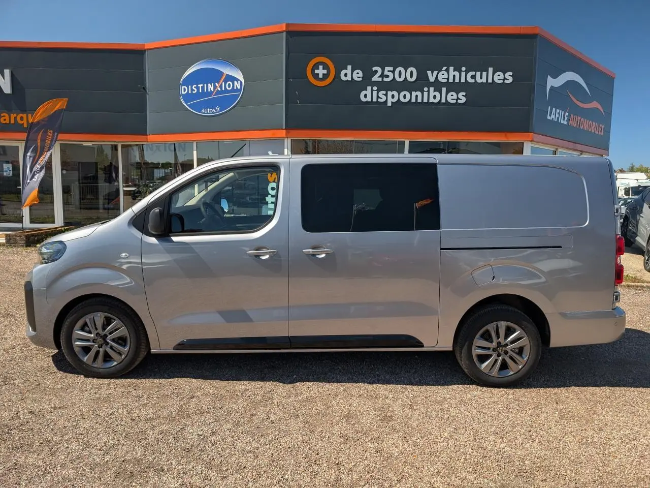 Profil côté gauche d'un Peugeot Expert Fourgon gris métallisé avec jantes alliage 17'' devant un concessionnaire.