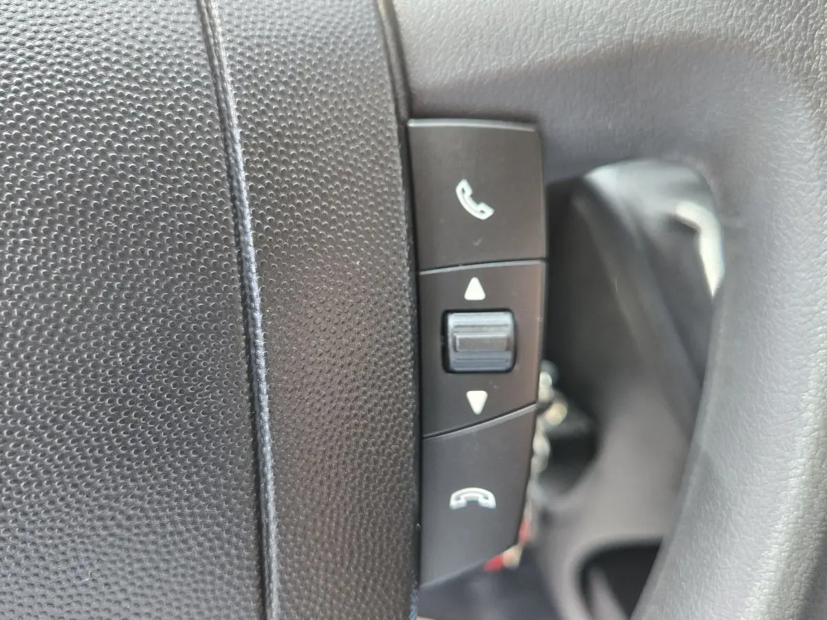 Gros plan sur les commandes de téléphone intégrées au volant noir du Fiat Ducato Fourgon blanc, version 2023.