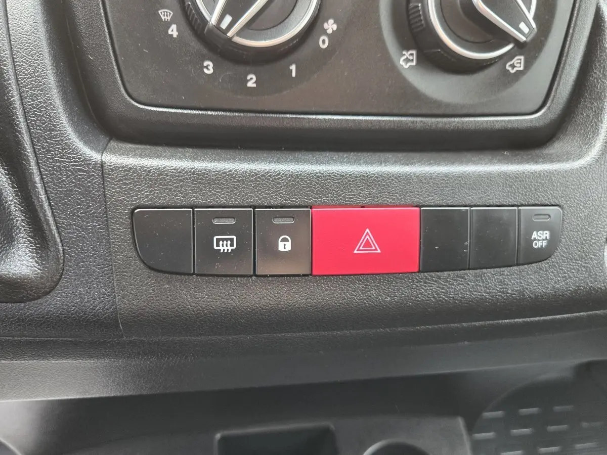 Gros plan sur les boutons de commande du tableau de bord noir du Fiat Ducato Fourgon blanc 2023, avec bouton rouge de warning.