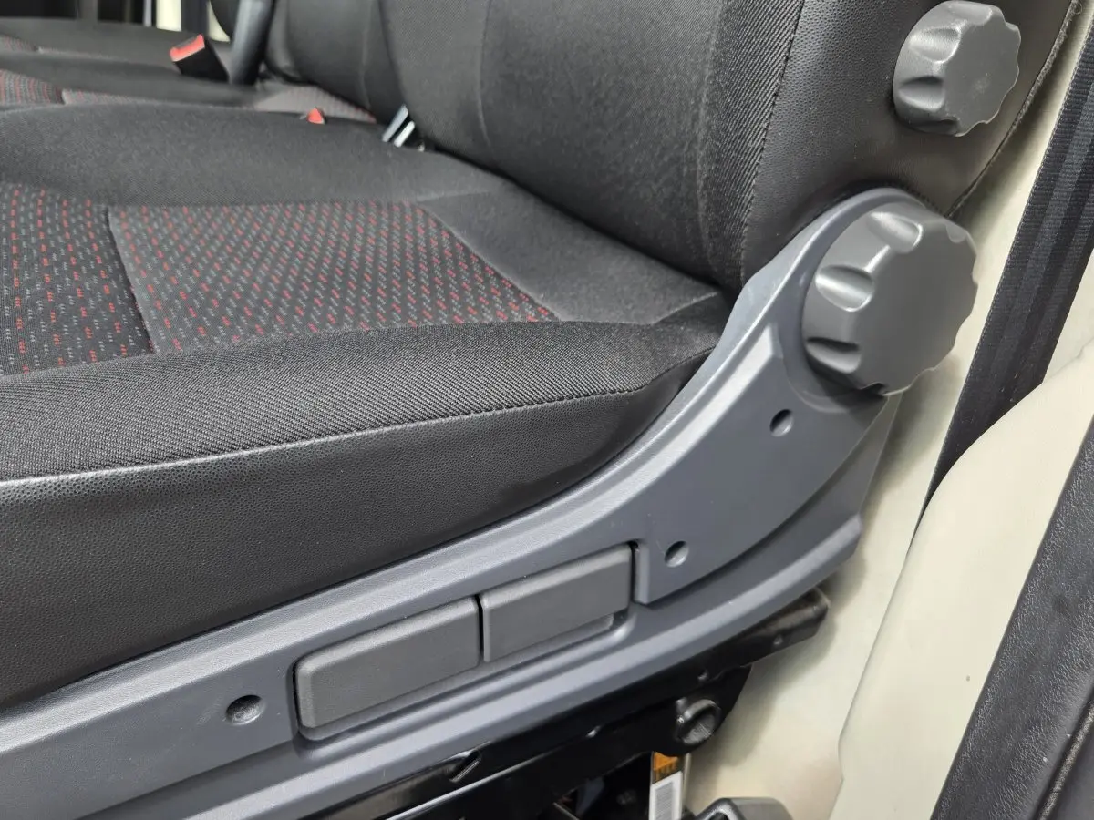 Gros plan sur le réglage manuel du siège conducteur en tissu noir avec motifs rouges du Fiat Ducato Fourgon blanc.