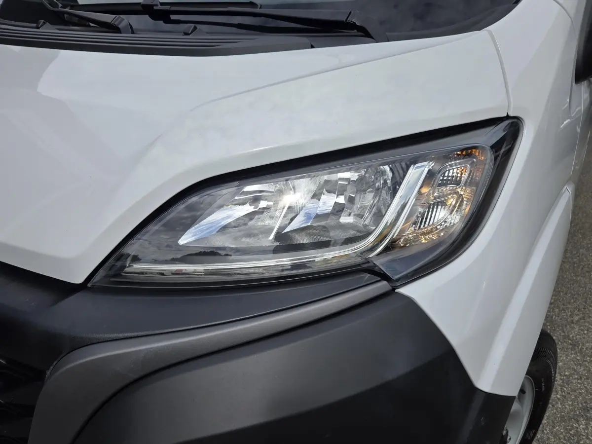 Gros plan sur le phare avant droit d’un FIAT Ducato Fourgon blanc avec pare-chocs noir.