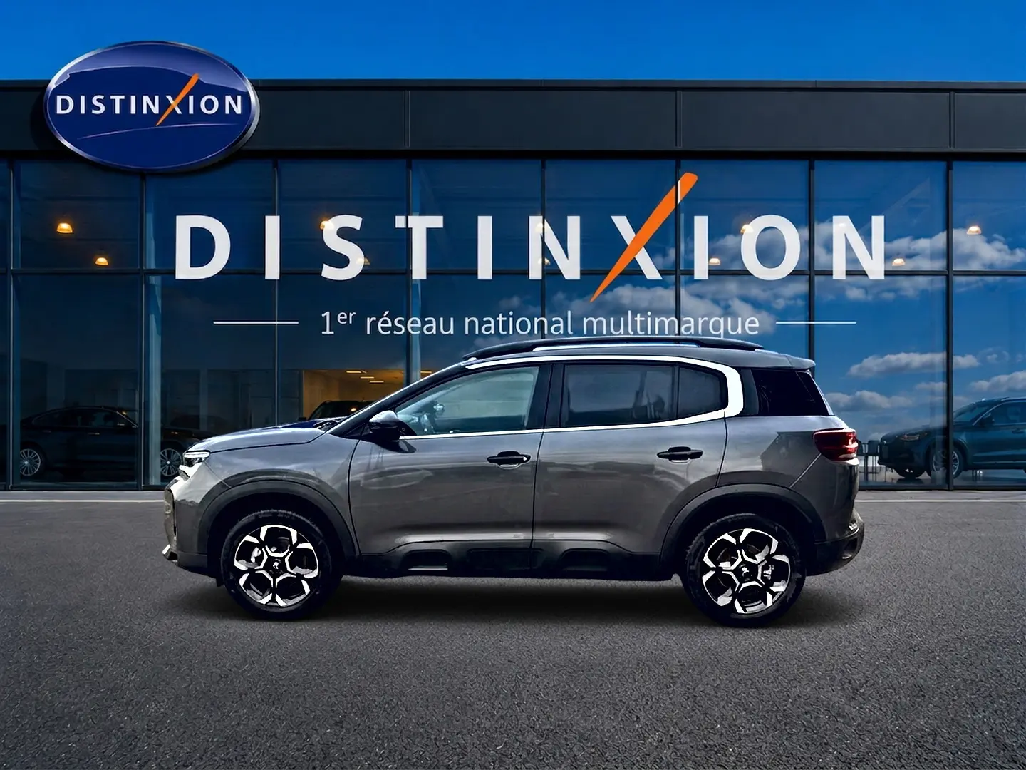 Profil droit du Citroën C5 Aircross gris platinium 2025, avec jantes alu et barres de toit visibles devant vitrine Distinxion.