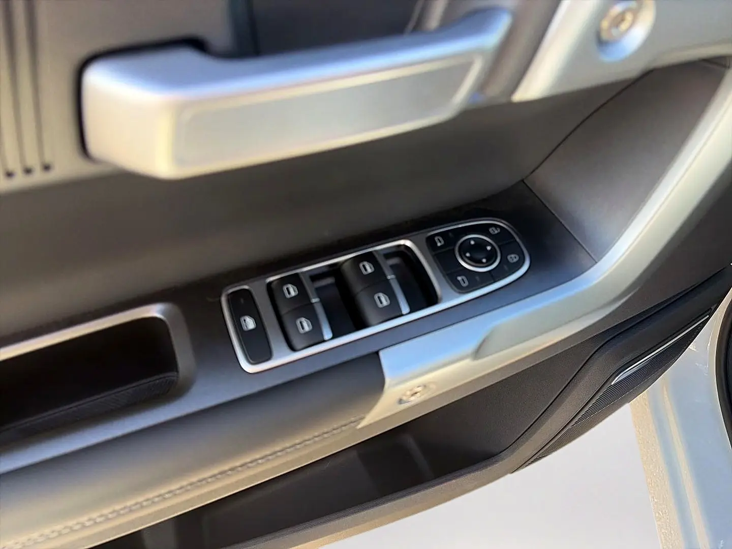 Gros plan sur la commande des vitres et rétroviseurs côté conducteur d’un JAECOO J7 blanc kaki.