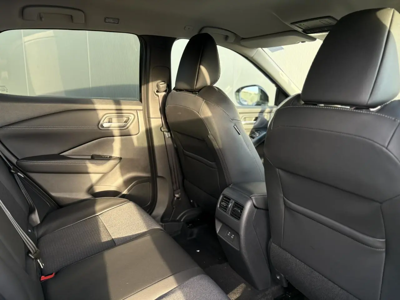 Vue intérieure arrière côté droit du Nissan Qashqai III noir, sièges en cuir et tissu avec aérateurs centraux.