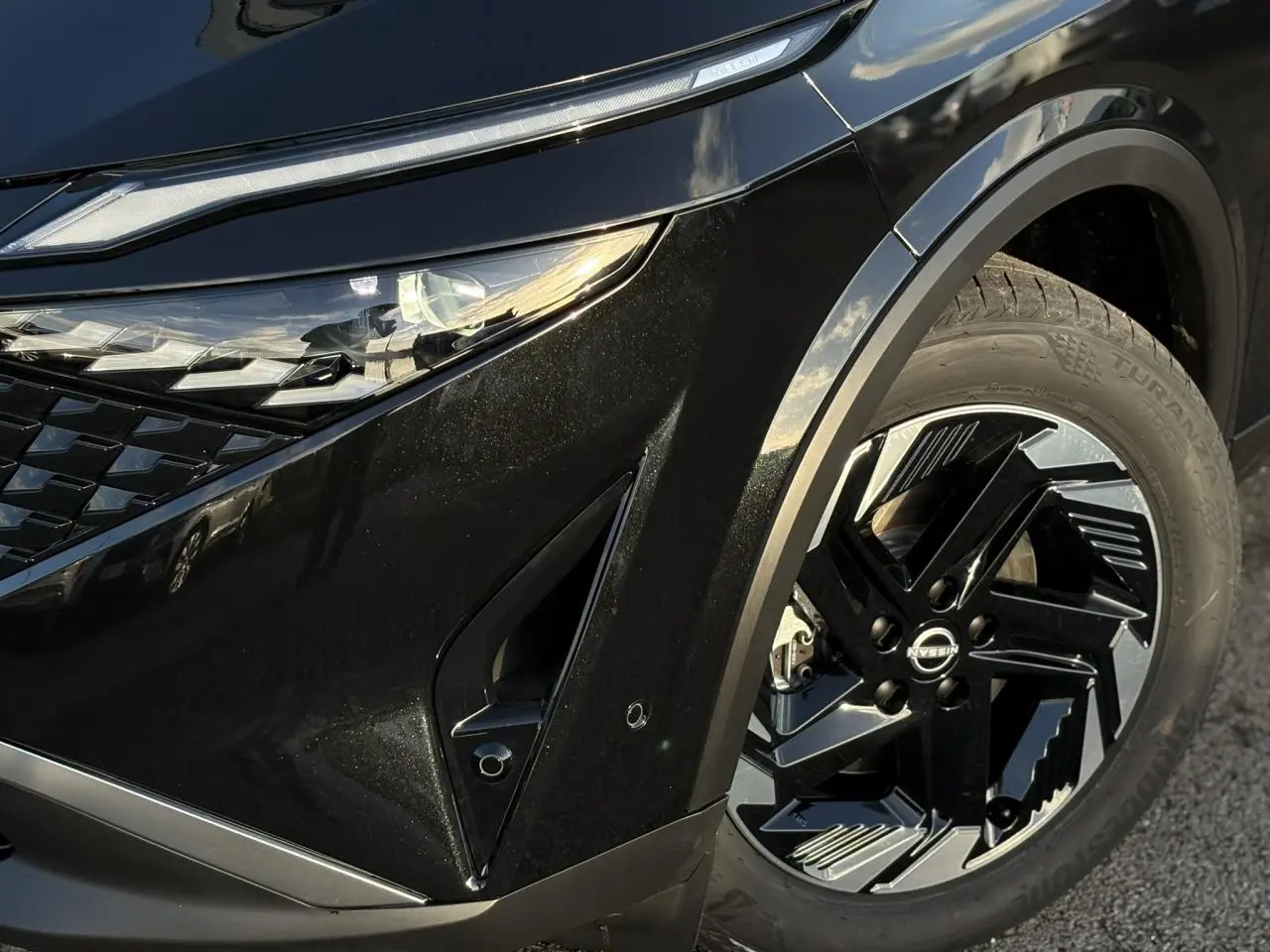 Gros plan sur l'avant droit noir du Nissan Qashqai 2025, mettant en valeur le phare LED et la jante alliage.