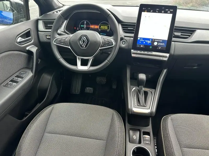 Vue intérieure avant du Renault Captur 2025, tableau de bord noir avec volant multifonction et écran tactile vertical.