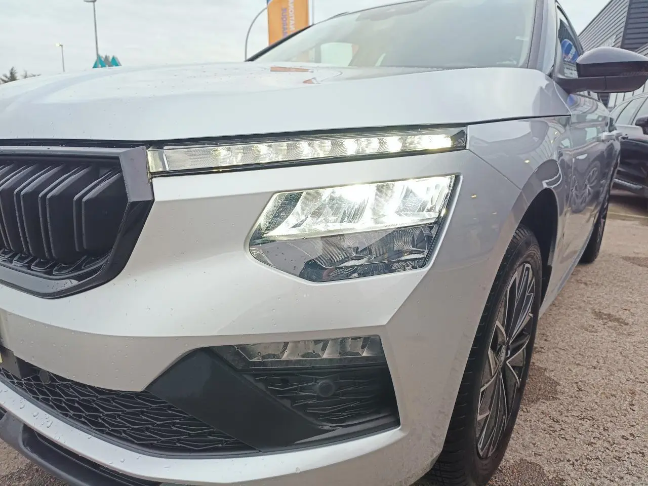 Vue 3/4 avant droit d'un Skoda Kamiq 2025 argent avec toit noir et phares LED allumés.