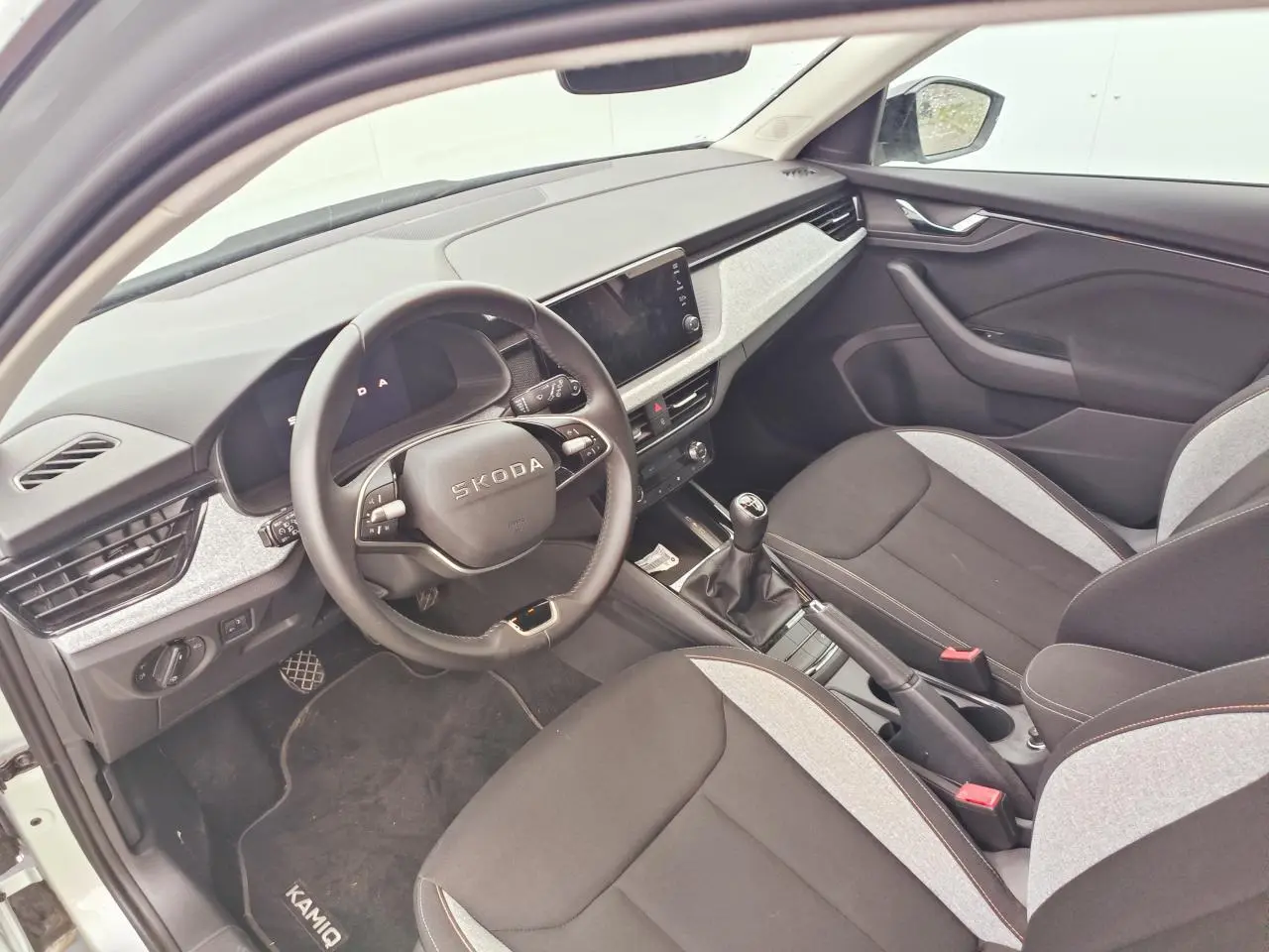 Intérieur de la Skoda Kamiq 2025 vu côté conducteur, sièges bicolores noirs et gris, volant multifonctions et boîte manuelle.