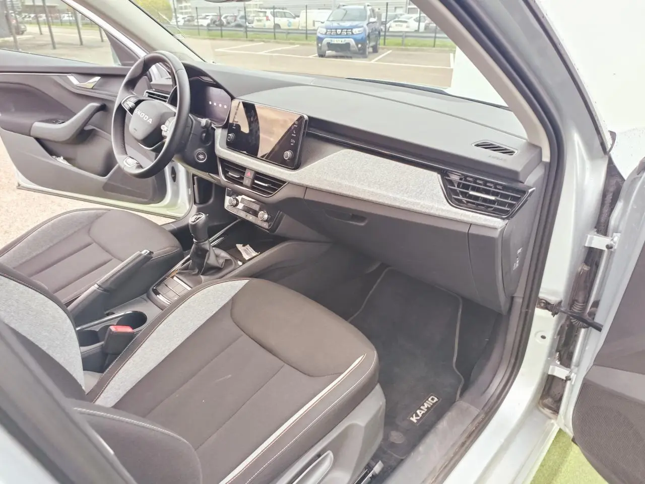 Intérieur avant droit d’une Skoda Kamiq 2025 gris argent avec tableau de bord moderne et boîte manuelle.