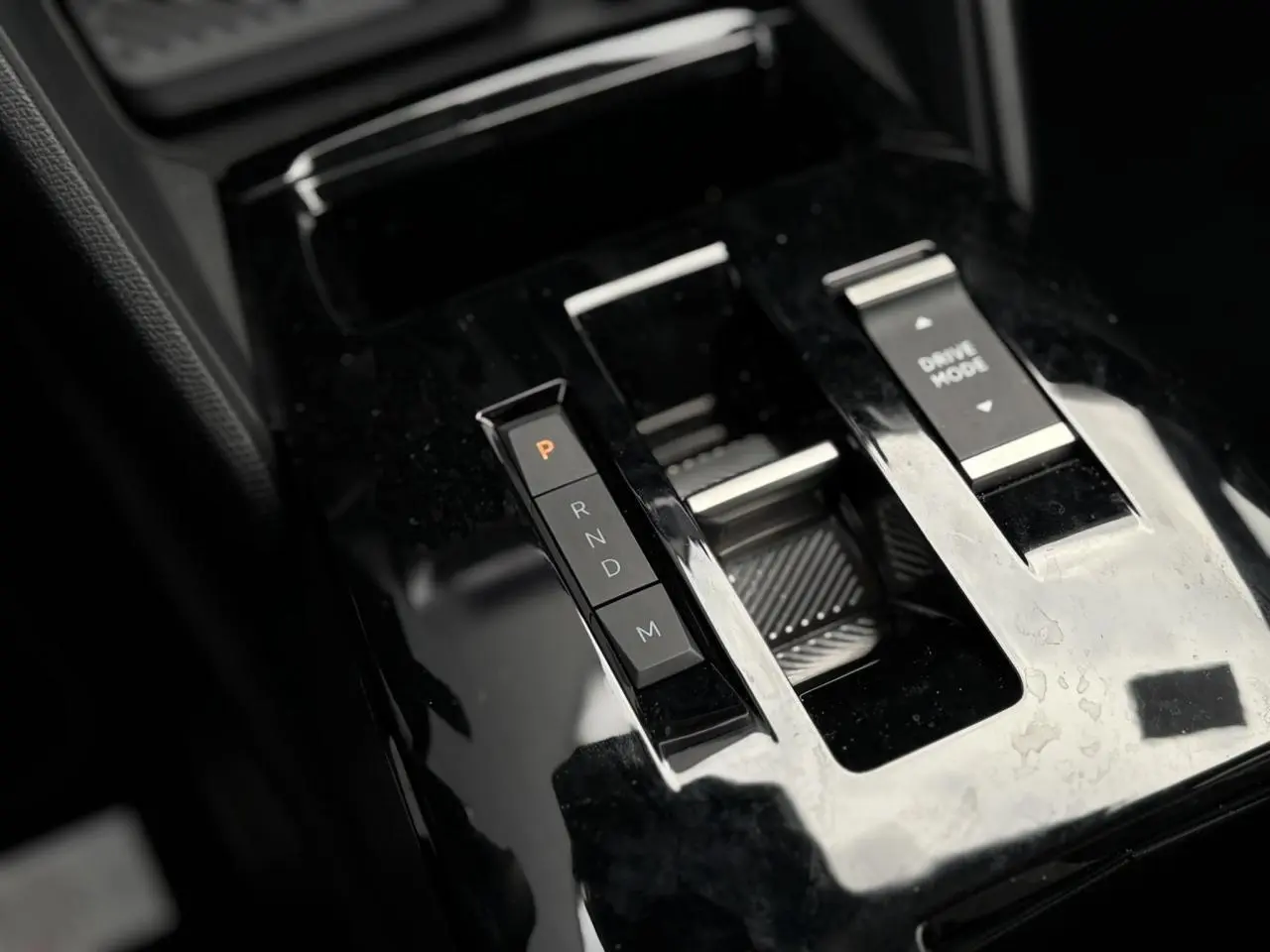 Gros plan sur la console centrale noire brillante de la Citroën C4 Hybrid 2025 avec sélecteur de boîte auto et bouton Drive Mode.