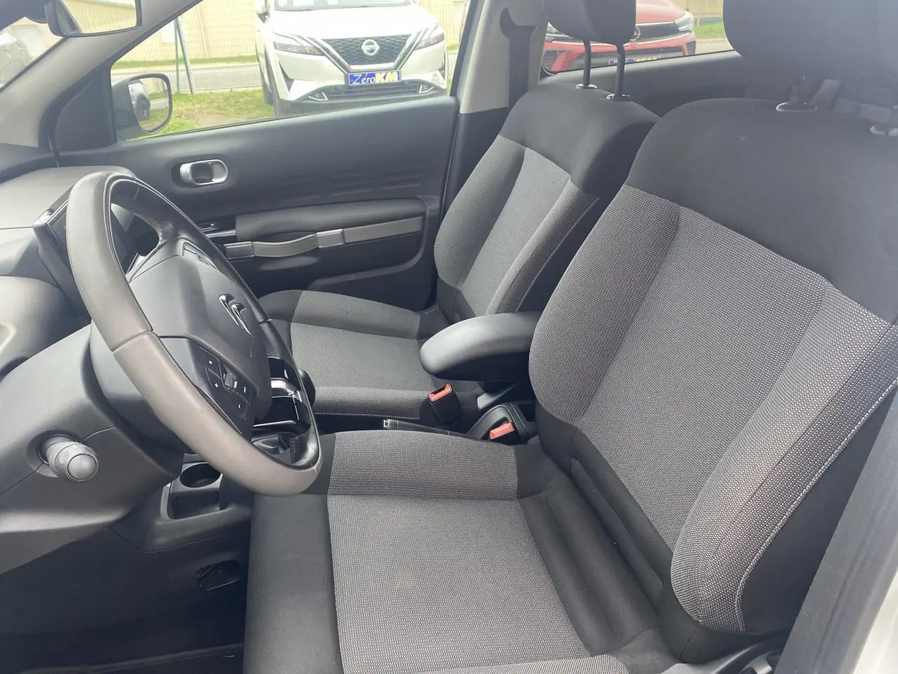 Vue intérieure côté conducteur de la Citroën C4 Cactus blanche de 2015, montrant sièges tissu gris et volant multifonction.