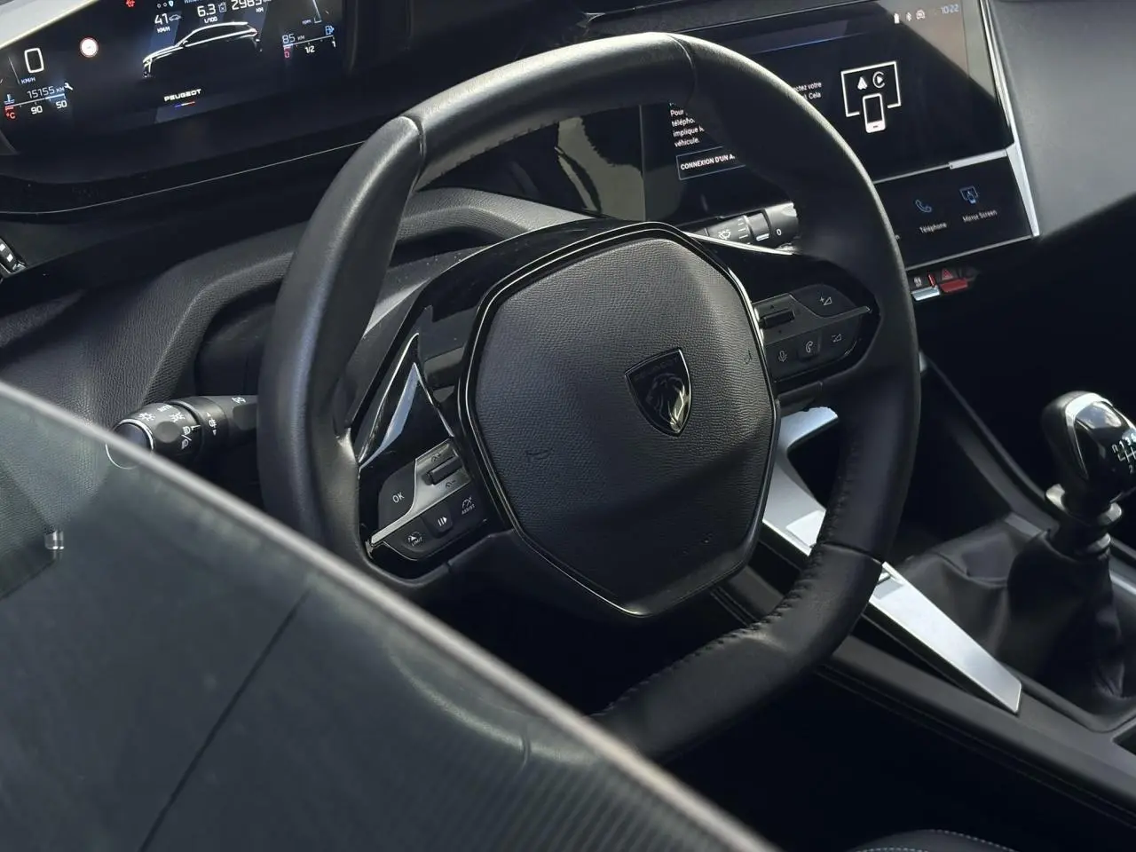 Vue intérieure rapprochée du volant cuir noir et levier de vitesse manuel de la Peugeot 308 2024.